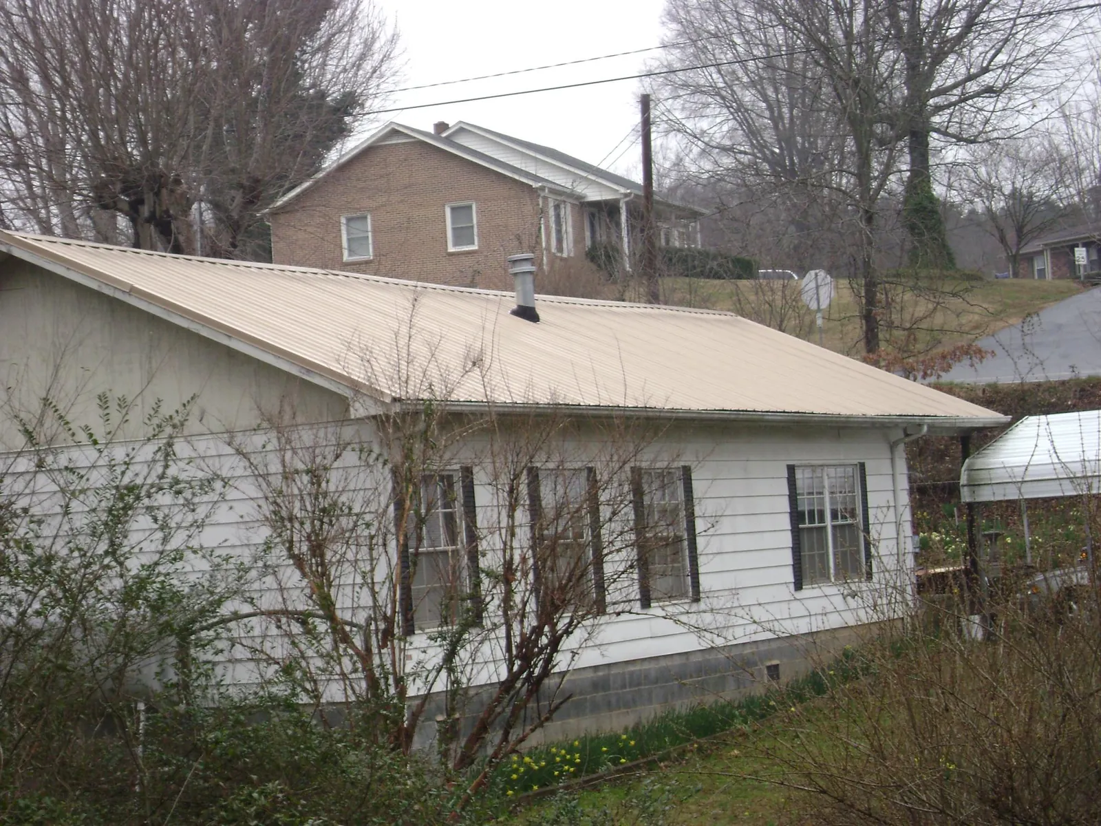 Tan metal roof on a white sided house set into a hillside — Commercial Roofing by Roofing Brothers in Archer